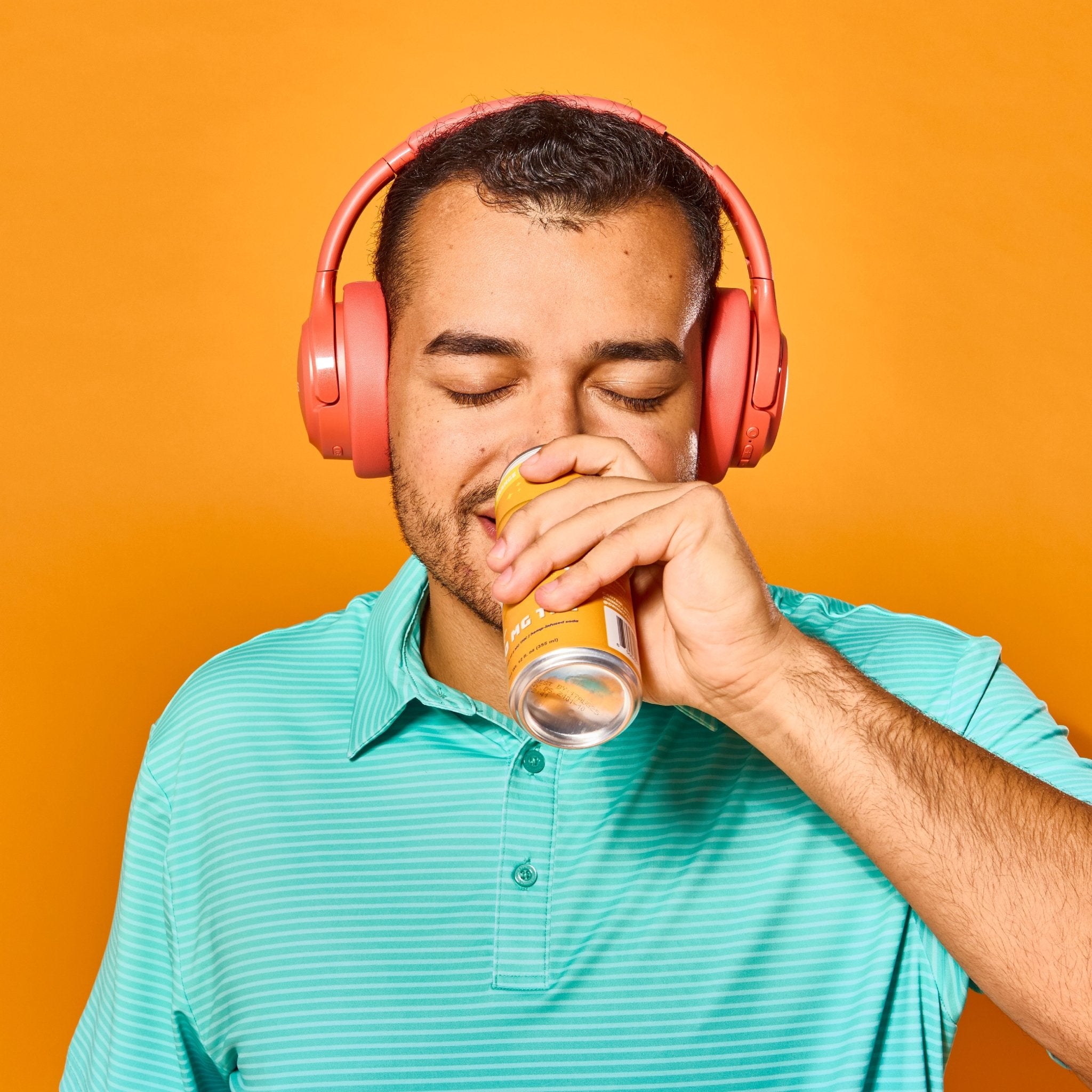 Man in a teal golf shirt drinking a 50 MG Cantrip THC Orange Soda. He's listening to music on orange headphones.