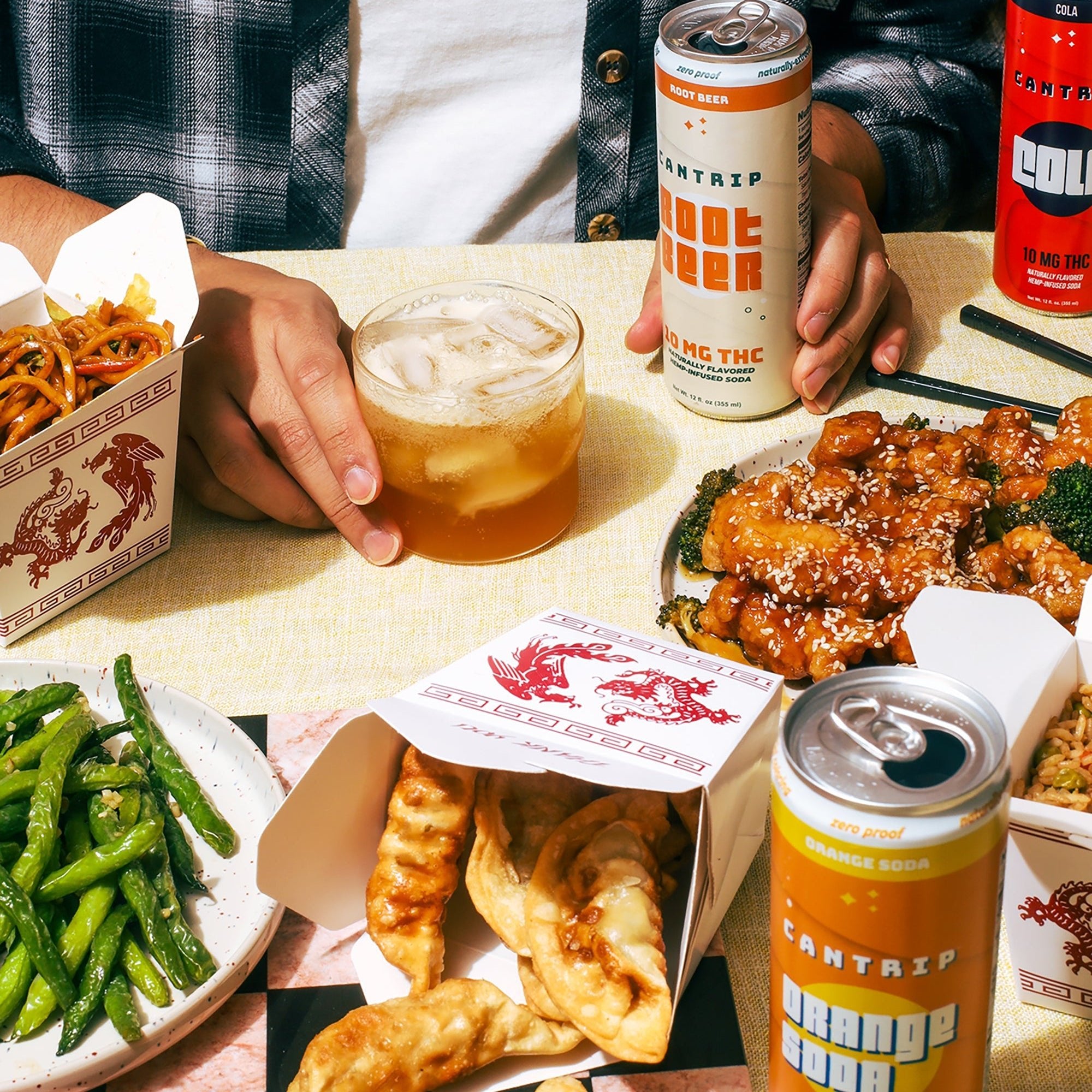Someone in a plaid shirt, seated at a table with Chinese takeout and Cantrip THC sodas.