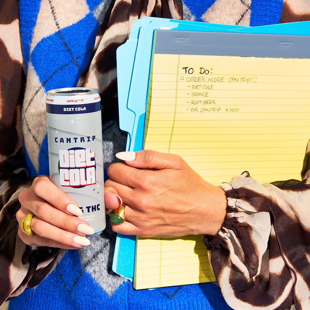 A person wearing an argyle sweater vest and holding a yellow legal pad with a to-do list in one hand, and a Cantrip THC Diet Cola in the other.