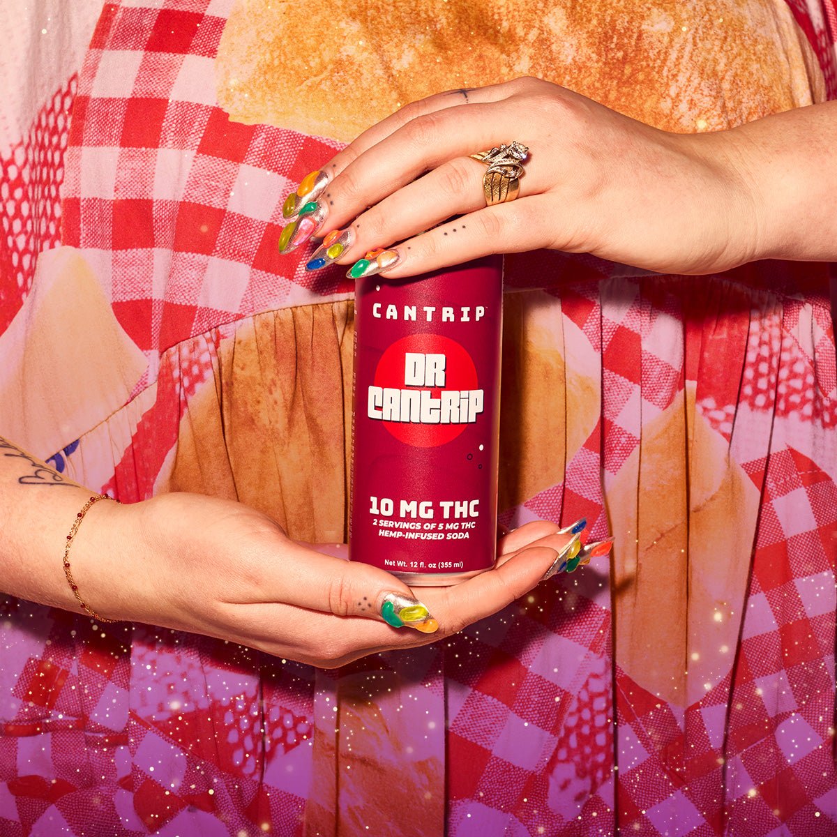 Person holding a red can labeled Dr Cantrip with a colorful manicure and a checkered dress