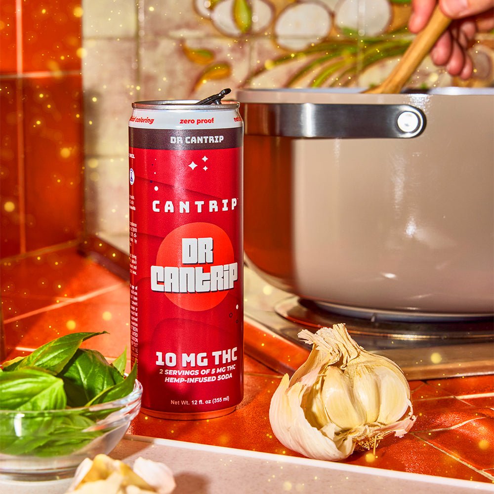 Red can of Dr Cantrip on a kitchen counter with garlic and herbs while cooking pasta