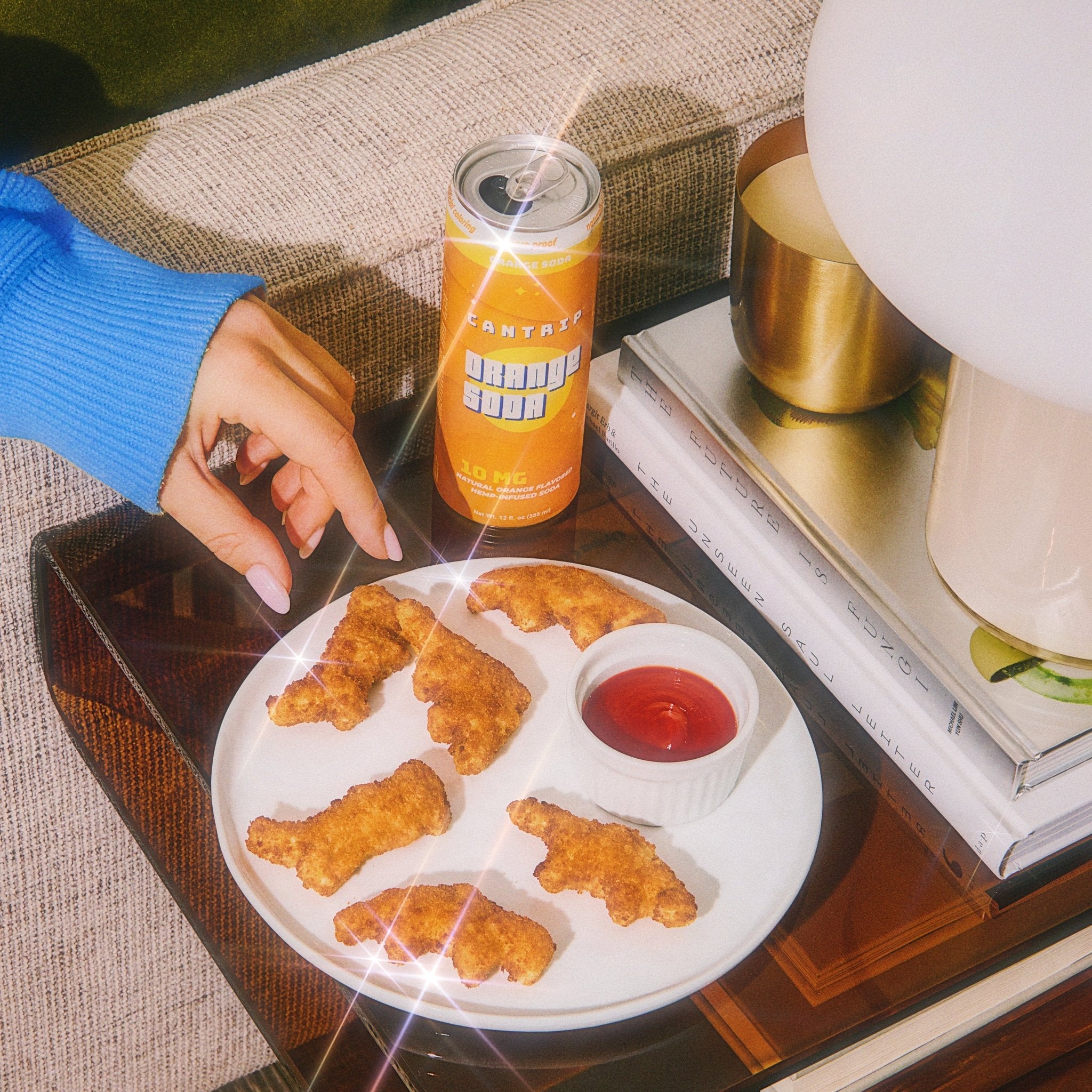 Cantrip Orange Soda THC can next to a plate of chicken nuggets with dipping sauce on a table
