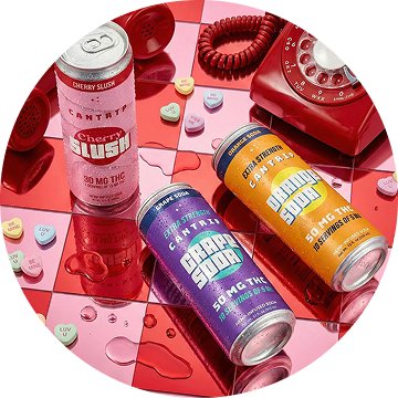 Cans of Cantrip Cherry Slush, Grape Soda, and Orange Soda on a red and pink checkerboard surface next to a red rotary dial phone and candy hearts.