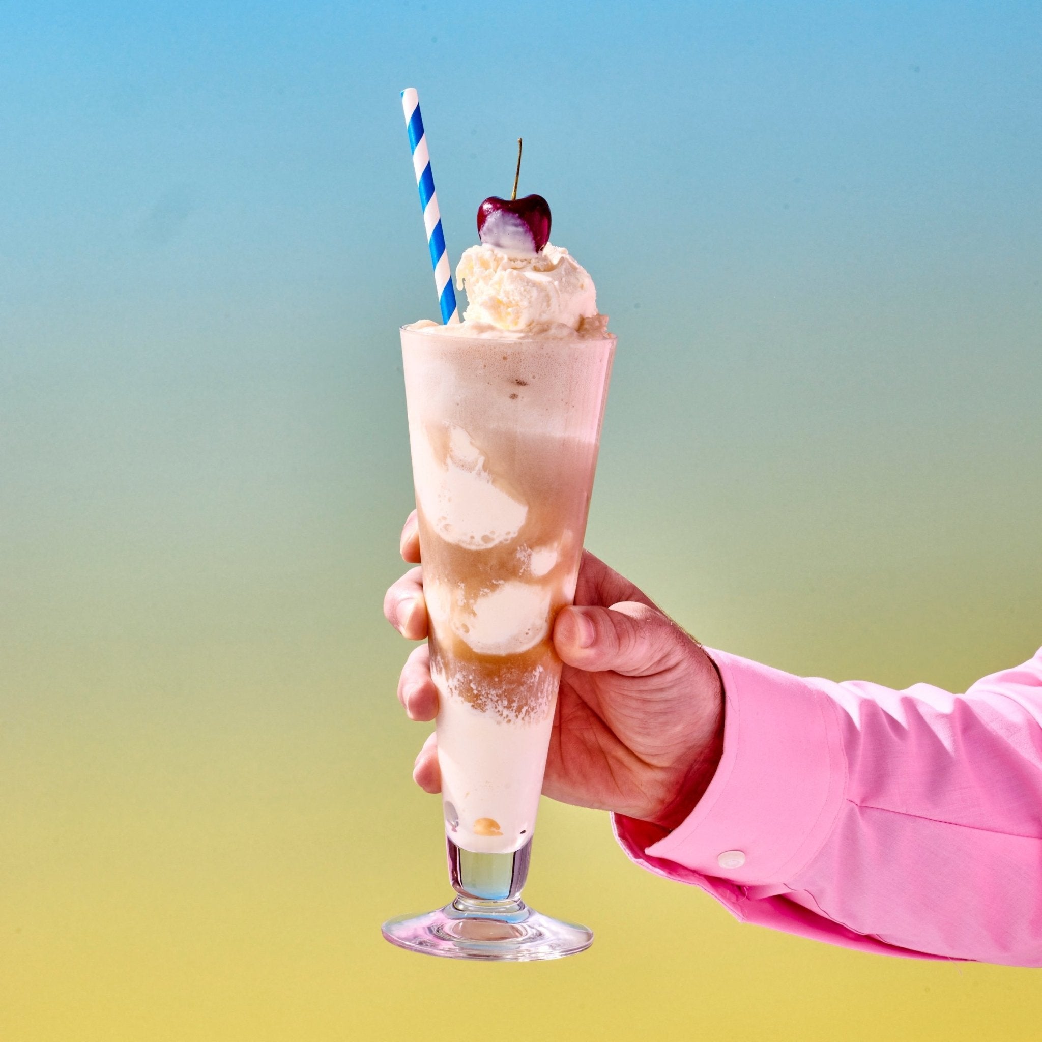 A hand holding a root beer float, made with Cantrip THC Root Beer and topped with a cherry. A blue and white straw has been inserted into the ice cream drink.